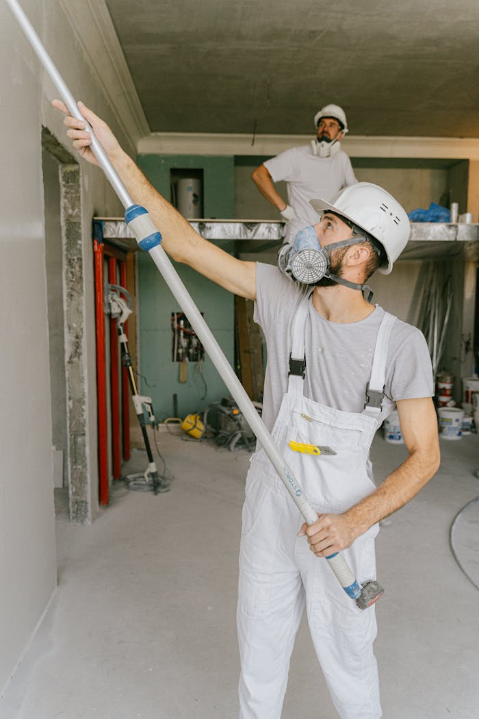 Two construction workers in safety gear are interior renovating, using a paint roller.